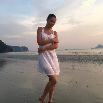 Doce bebê Lovenia Lux posando com um vestido branco na praia